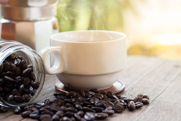 Uma xícara de canecas de café expresso quente e grãos de café torrados com panela moka colocada no fundo do chão de madeira, manhã de café, foco seletivo - Foto, Imagem