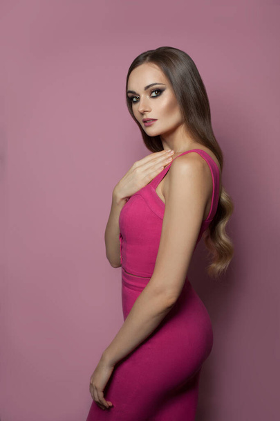 Beautiful fit healthy model woman with long hair in pink dress standing on pink background - 写真・画像