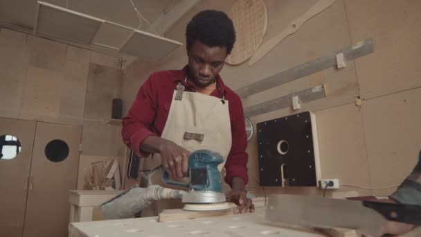Tiro medio del joven manitas africano que trabaja con la máquina de pulir a mano en taller de carpintería - Imágenes, Vídeo