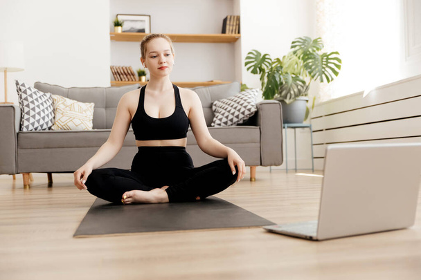 Young attractive woman practicing yoga at homeand uses laptop, yoga for beginners online - Φωτογραφία, εικόνα
