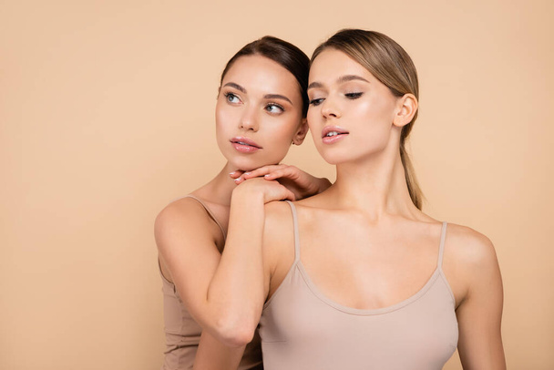 young woman leaning on shoulder of pretty friend while looking away isolated on beige - Photo, Image