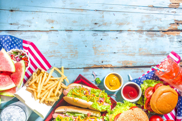 Fourth of July, Memorial Day, USA Independence Day concept. Patriotic, American traditional food. Picnic party with watermelon, burgers, hot dogs, drinks, blue wooden outdoor table background - 写真・画像