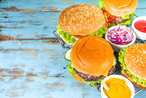 Assortiment de hamburgers américains traditionnels, avec des sauces et des frites sur un fond bleu en bois. Pique-nique, arrière-plan de la nourriture extérieure, espace de copie vue du dessus  - Photo, image
