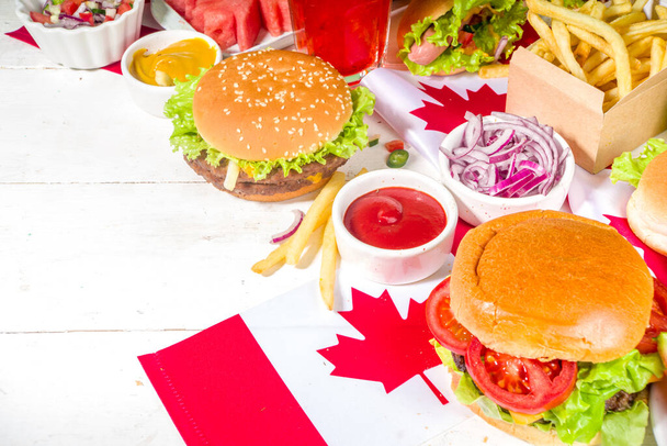 Set of various Canada Day bbq food. Picnic party table with maple leaf shaped watermelon, flags, burgers, hot dogs, fries and sauces, cold drinks, white table with red decor, top view copy space - Photo, Image