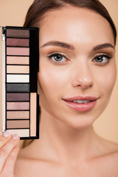 pretty woman with perfect skin and natural makeup near eye shadows palette isolated on beige - Фото, изображение