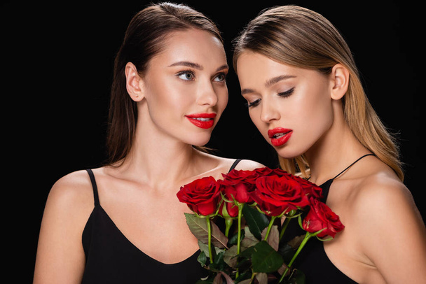 jovem mulher olhando para amigo encantador com rosas vermelhas isoladas em preto - Foto, Imagem