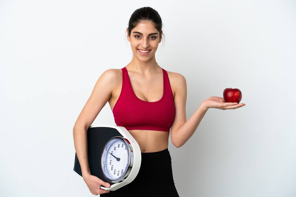 Young caucasian woman isolated on white background with weighing machine and with an apple - Photo, Image