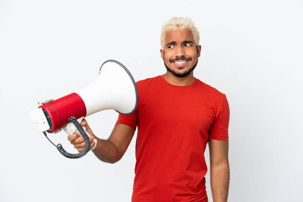 Young Colombian handsome man isolated on white background holding a megaphone with stressed expression - Valokuva, kuva