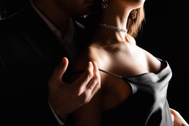 vista recortada de mujer sensual en vestido de seda con mano masculina en hombro aislado en negro - Foto, imagen