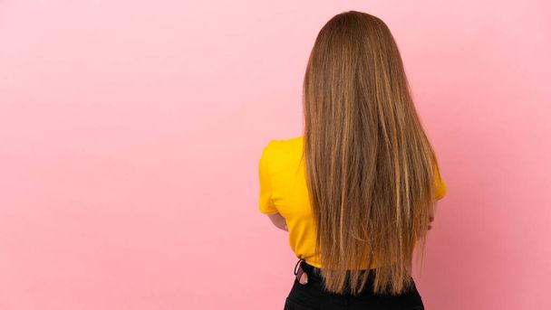 Teenager dívka přes izolované růžové pozadí v zadní poloze - Fotografie, Obrázek