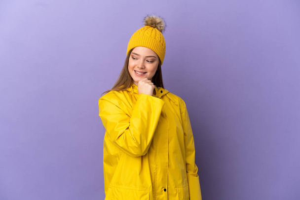 Teenager girl wearing a rainproof coat over isolated purple background looking to the side and smiling - Foto, immagini