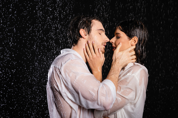 passionate sexy couple in wet clothes standing in rain drops on black background - Photo, Image