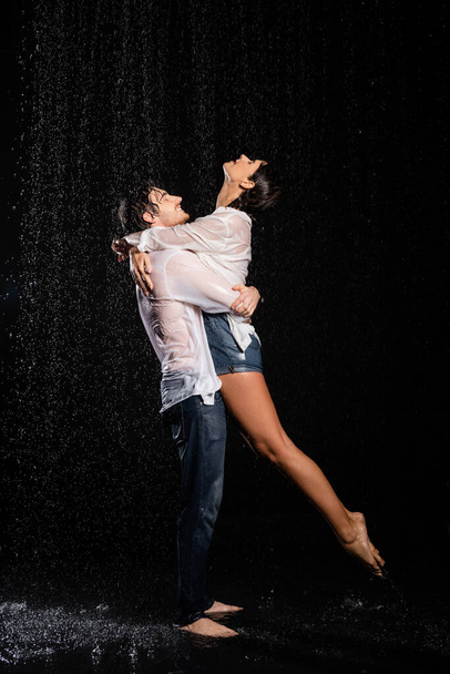 wet happy and passionate romantic couple hugging in rain drops on black background - Foto, Bild