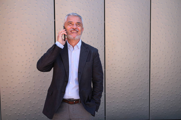 Ώριμος και χαρούμενος επιχειρηματίας μιλώντας στο τηλέφωνο σε εξωτερικούς χώρους - Φωτογραφία, εικόνα