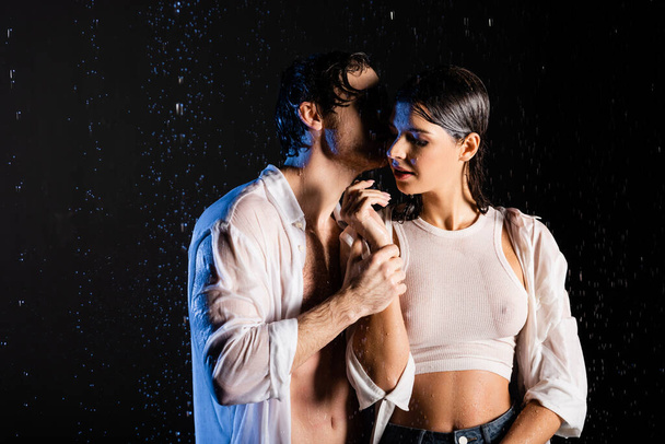 wet passionate couple holding hands and hugging in rain drops on black background - Fotografie, Obrázek