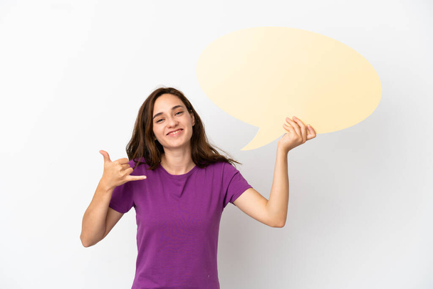 Young caucasian woman isolated on white background holding an empty speech bubble and doing phone gesture - Foto, afbeelding