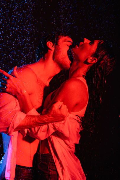 filtros de colores rojo y azul imagen de pareja romántica sexy mojada besándose apasionadamente en gotas de agua sobre fondo negro - Foto, imagen
