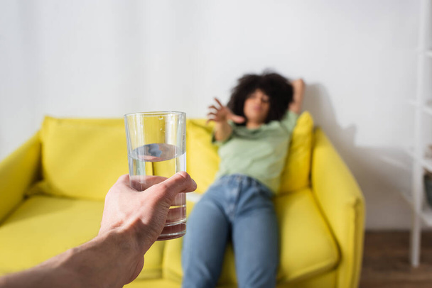blurred african american woman with outstretched hand reaching glass of water in male hand - Foto, Bild