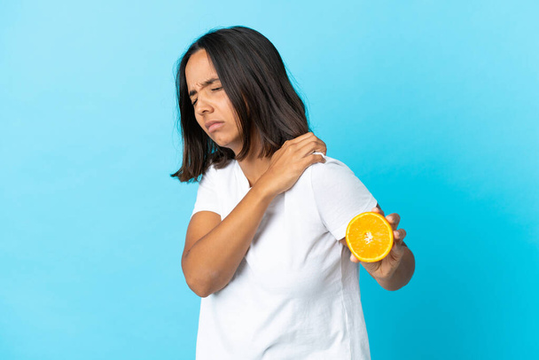 Fiatal ázsiai lány kezében egy narancs elszigetelt kék háttér szenved a fájdalom a vállban, mert tett egy erőfeszítést - Fotó, kép