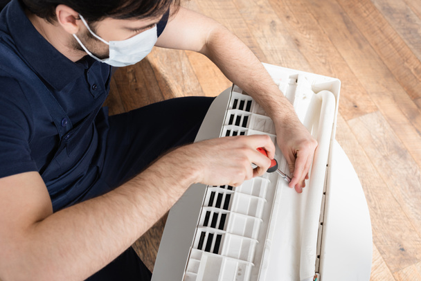 high angle view of handyman in medical mask fixing broken air conditioner  - Photo, Image