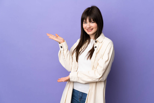 Young Ukrainian woman isolated on purple background extending hands to the side for inviting to come - Фото, изображение