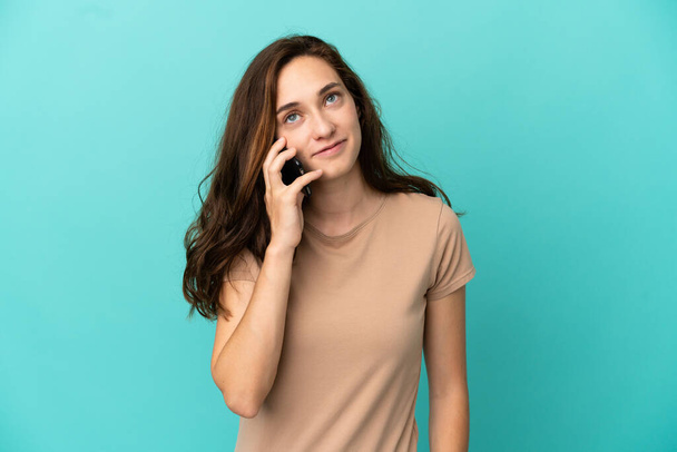 Young caucasian woman isolated on blue background keeping a conversation with the mobile phone with someone - Foto, Imagen