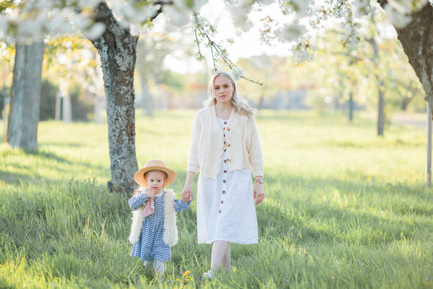 Una hermosa madre joven con su hija pequeña descansan en un picnic en el jardín floreciente. Flores blancas. Primavera. - Foto, Imagen
