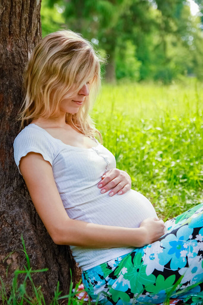 Happy pregnant woman on nature in a park background - Fotó, kép