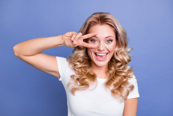 Photo of young beautiful attractive pretty smiling excited girl showing v-sign on eye isolated on blue color background - 写真・画像