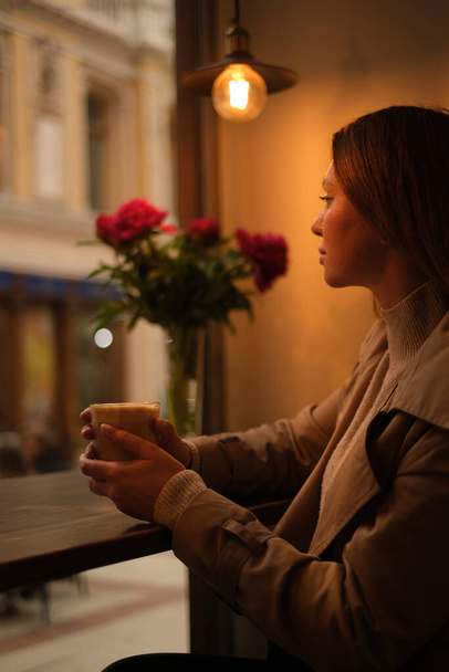 beautiful young woman drinking coffee in a cozy coffee shop overlooking the historic buildings in the baroque style. - Photo, Image