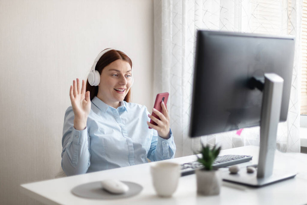 Hezká mladá žena používající mobilní telefon při práci s PC doma. Online videokonference. - Fotografie, Obrázek