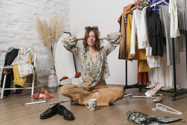 Een gestresste jonge vrouw in een rommelige kamer vol kleren. Niets om te dragen concept. - Foto, afbeelding