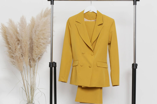 Des vêtements pour femmes. Porte-vêtements, blazer jaune et pantalon dans l'atelier de mode. - Photo, image