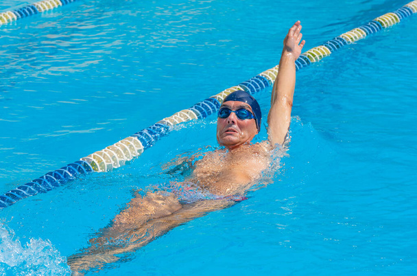 an adult, former swimmer, trains in a public swimming pool, with sun - Valokuva, kuva