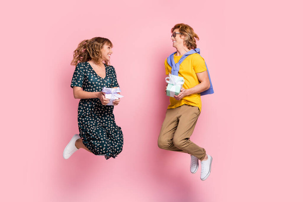 Full size profile photo of optimistic funny couple jump hold present wear colorful clothes isolated on pastel pink background - Fotó, kép