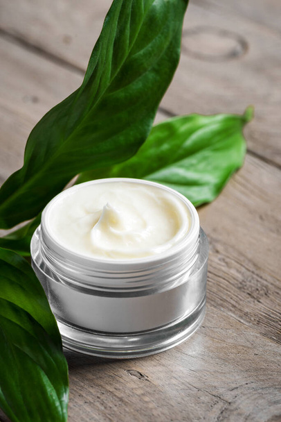 Jar of cosmetic cream and green leaves on wooden table. Natural eco beauty and organic skin care concept. - Foto, Imagen