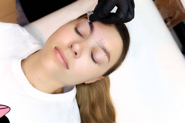 el maquillador permanente trata la piel del cliente alrededor de los ojos después del procedimiento del tatuaje - Foto, Imagen