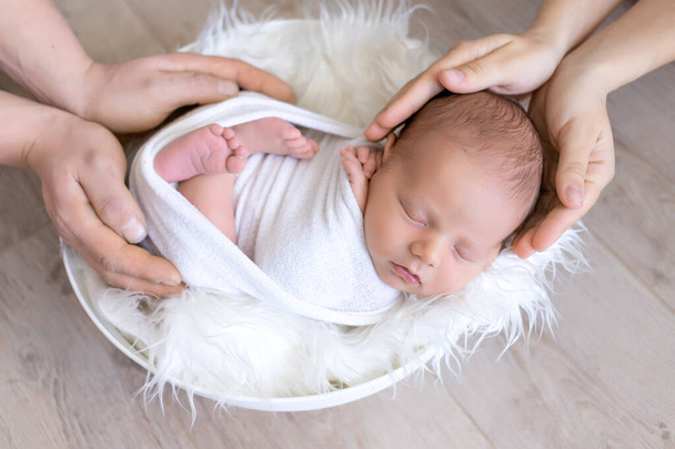 un nouveau-né entre les mains des parents, un bébé dormant entre les mains de son père et de sa mère sur fond blanc, une famille heureuse - Photo, image