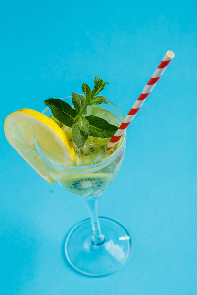 Kiwi cocktail garnished with lemon and mint in a glass on a napkin against a blue background. Vertical photo - Фото, зображення