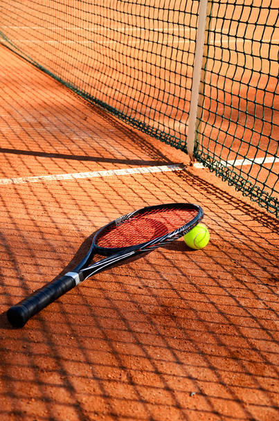 Bola de tênis e raquete estão perto da rede vertical
 - Foto, Imagem