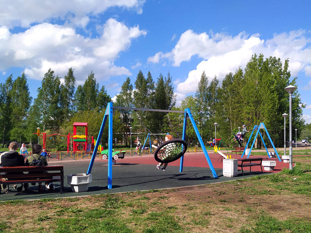 Saint Petersburg, Russia-May, 2021. Children swing on a swing, a man and a woman sit on a bench in the playground. Walk people on a sunny spring day off. - Фото, зображення