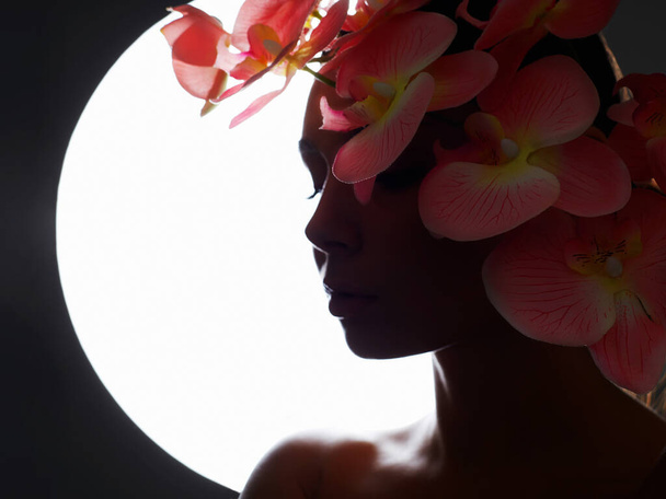 Hermosa silueta de mujer joven con flores. Retrato de belleza de niña con flor de orquídea - Foto, Imagen