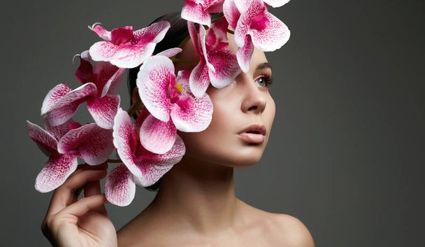 Nainen ja kukat. Kauneus muotokuva tyttö orkidea kukka. Puhdas iho Face, hoito - Valokuva, kuva