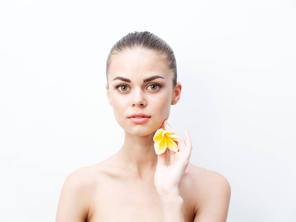 portrait of young woman with bared shoulders and flower near face - Foto, Bild