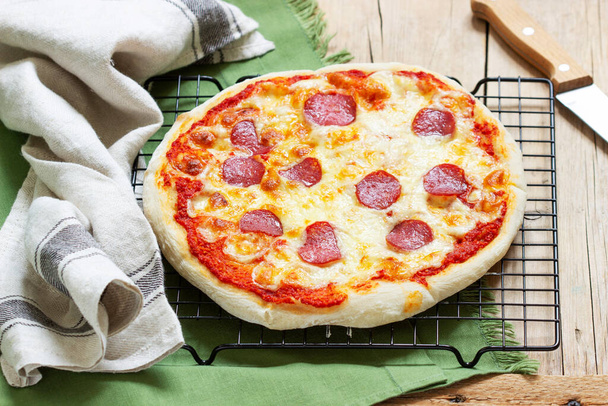 Házi készítésű pizza paradicsomszósszal, gyógynövényekkel, kolbásszal és sajttal egy fa asztalon. - Fotó, kép