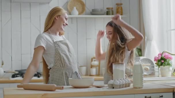 Dospělý krásný matka blondýnka hospodyňka maminka a teenager dívka dítě dcera nosit zástěry vaření společně v kuchyni, školačka radovat skákání z úspěchu triumf baví dělá vítězství gesto - Záběry, video