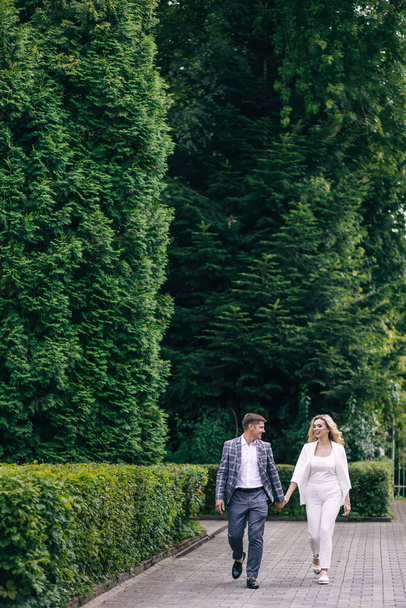 Loving groom and cute bride in suits with long hair are walking in nature. smiling newlyweds. - Zdjęcie, obraz