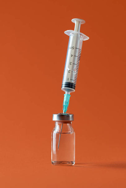 Butelka z lekiem i strzykawka z igłą minimalistyczna na pomarańczowym tle. Fiolka ze szczepionką izolowana na kolorowym tle. - Zdjęcie, obraz