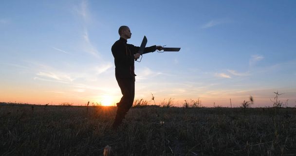 Silhouette of young male kung fu fighter practising alone in the fields during sunset - Foto, Bild