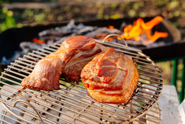 Grilled bacon on the background of the grill. Smoked bacon, fire burns in the back - Фото, изображение